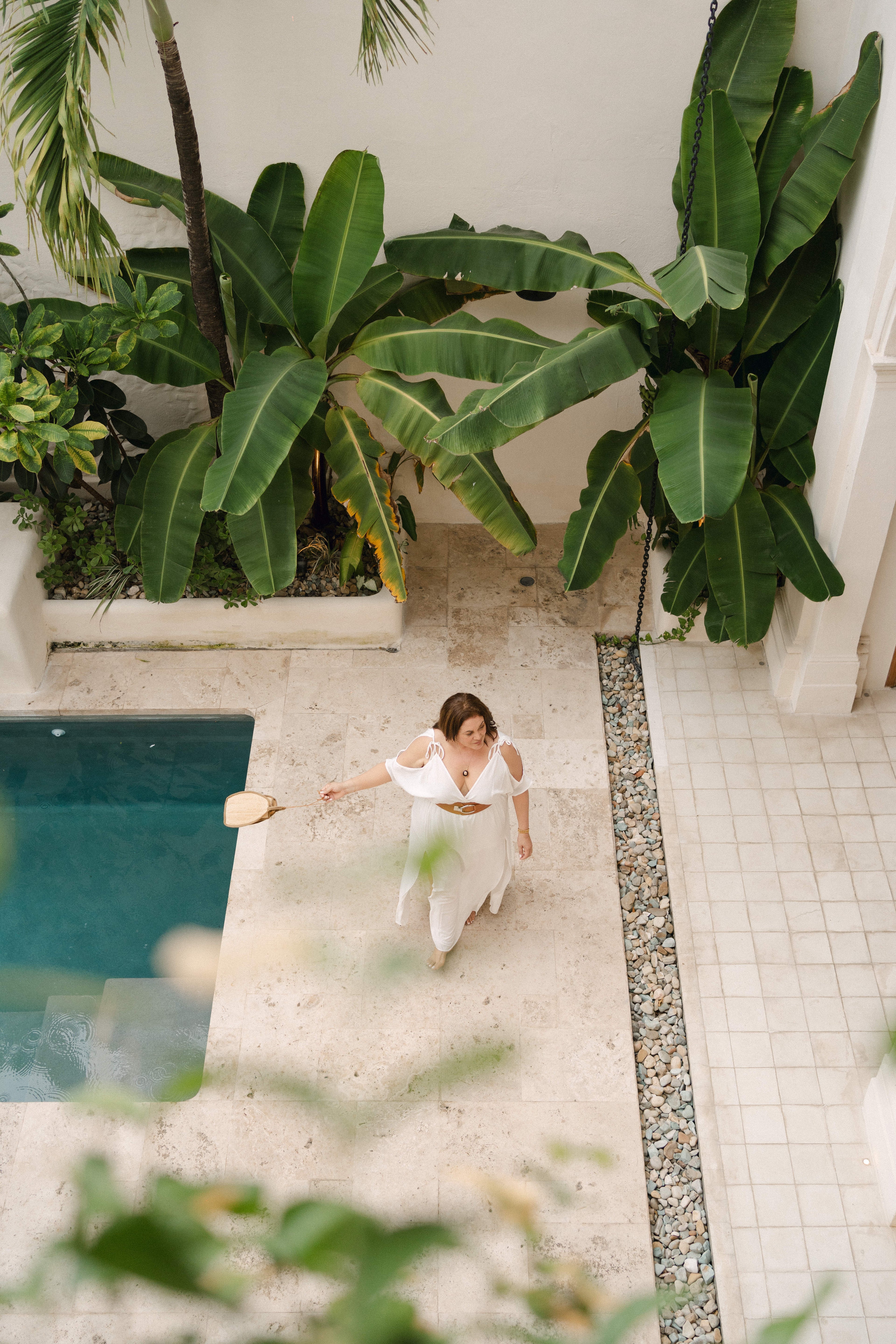 Woman in a white dress standing by a pool with tropical plants around